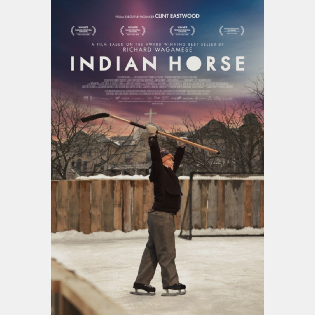 Movie cover for film Indian Horse, which has a boy holding a hockey stick in the air above his head, while skating on ice outside, with a residential school’s rooftop cross in the background.